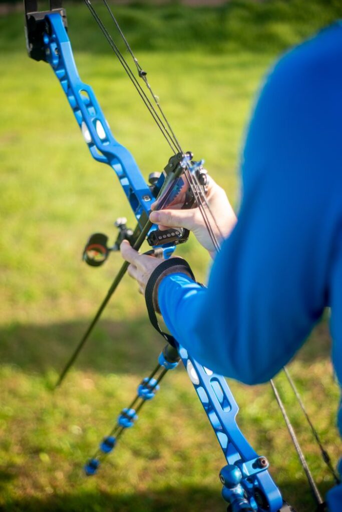Person adjusting a blue archery bow outdoors, showcasing precision and focus.