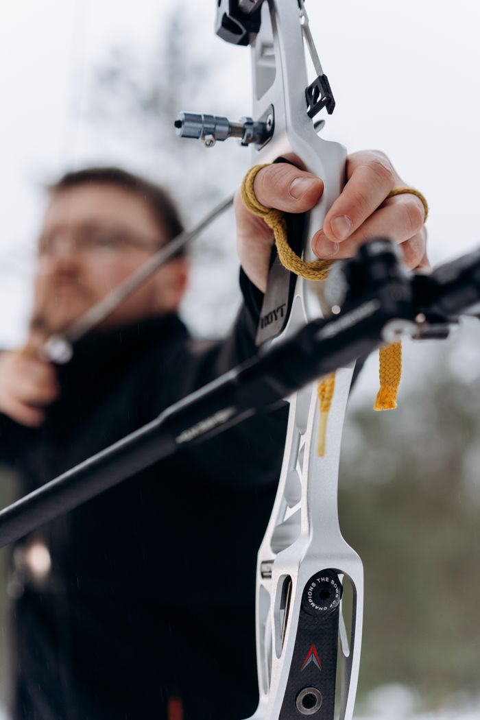 A man precisely aims a recurve bow, demonstrating focus and skill in archery.