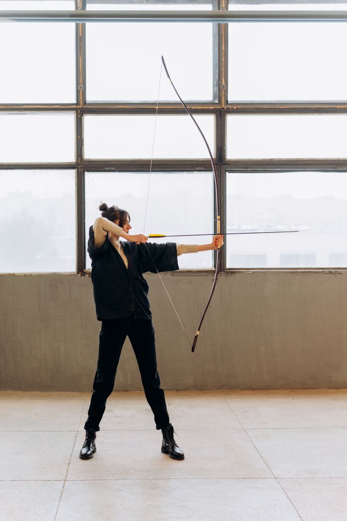 Woman practicing archery indoors, showcasing focus and skill with a bow and arrow.