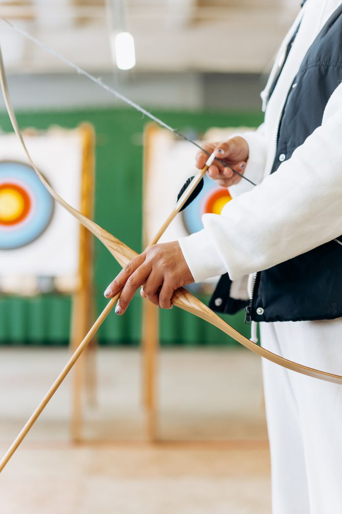 An archer pulls back the bowstring, aiming at a distant target. Focus on hands and equipment.